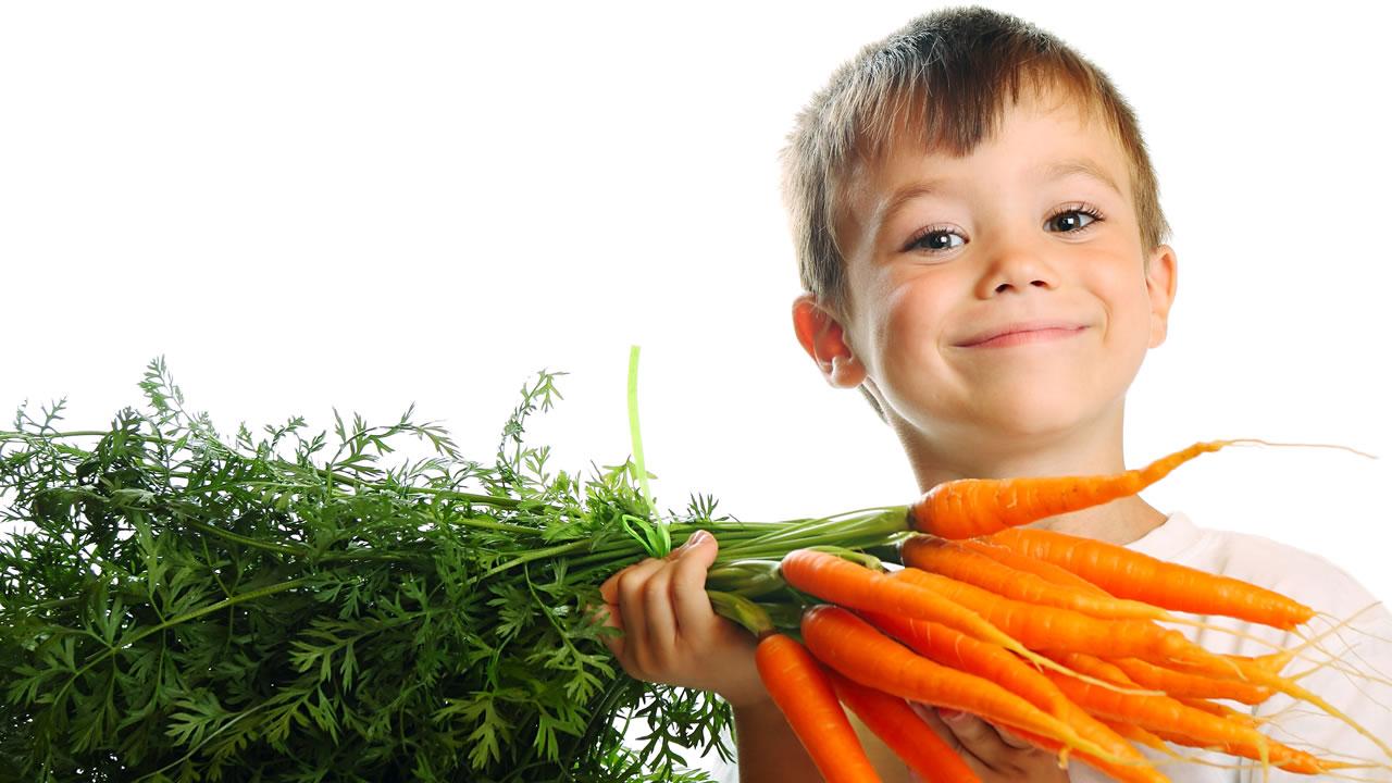 Child holding up carrots.